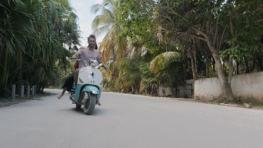 Man and woman riding a moped down a street