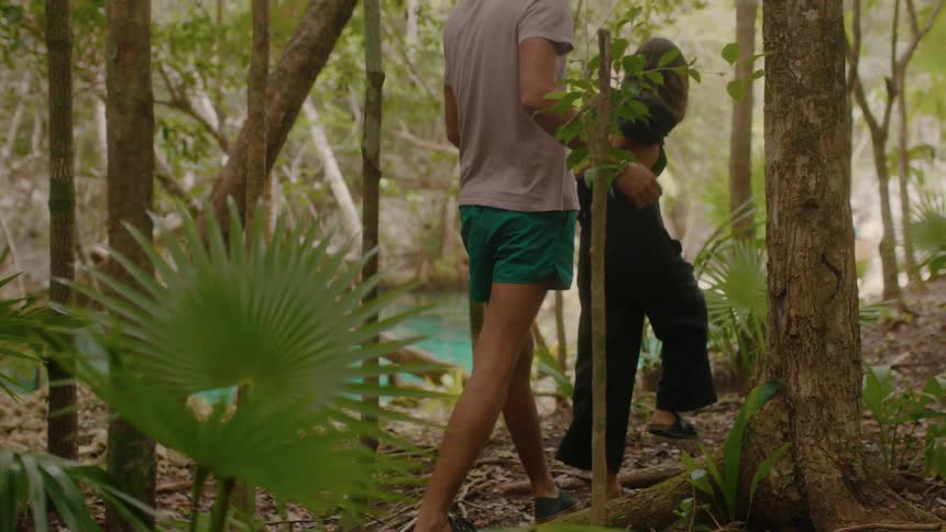 A couple are walking toward a natural pool in a forest during the day