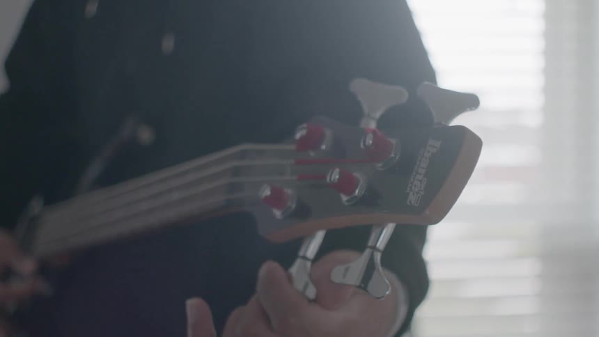 A man is tuning his guitar inside in daylight