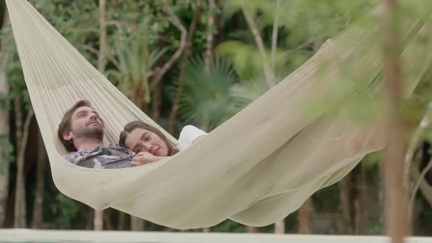 A man and woman are laying in a hammock together