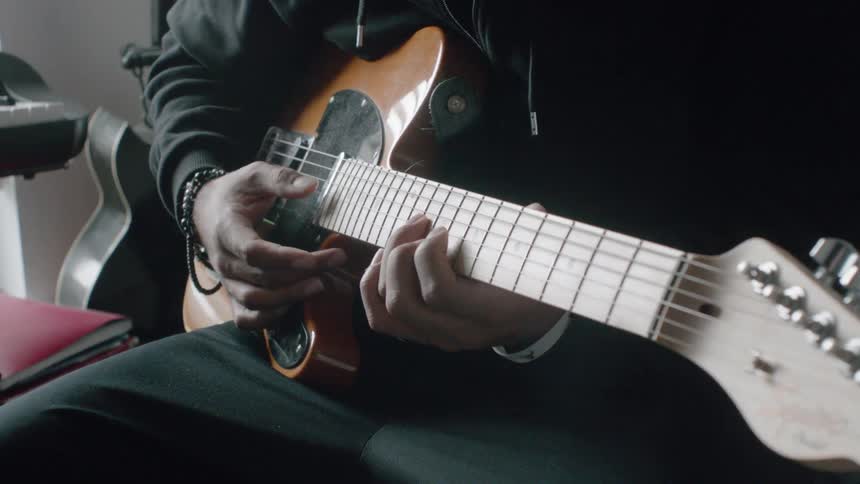 Person strums a guitar and sits next to a keyboard