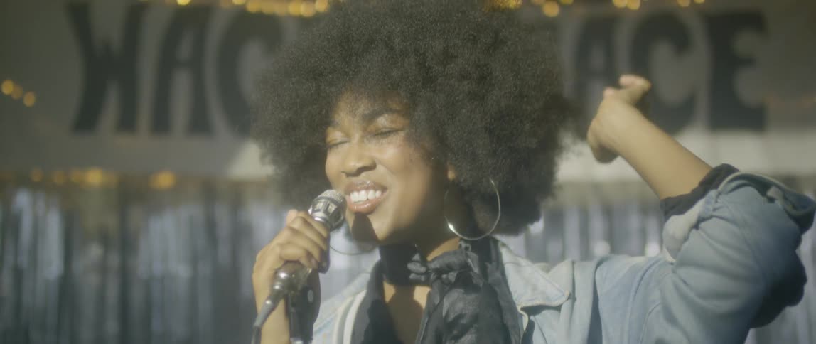 A woman miles and gestures as she sings
