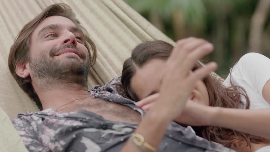 A man and woman in a hammock smile and hold hands