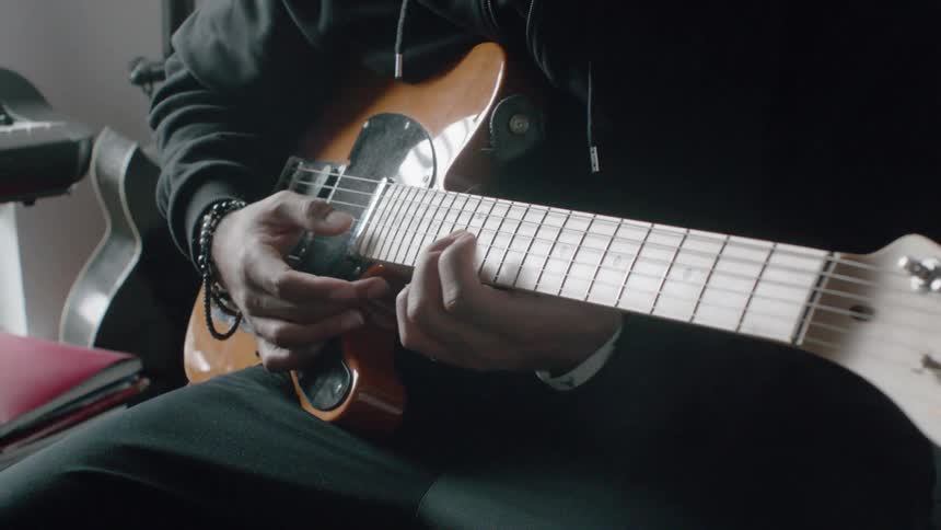 A man is playing a guitar inside during the day