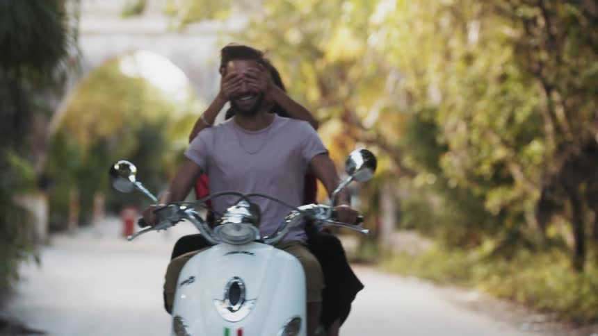 A man and woman smile and laugh as they ride on the motorcycle