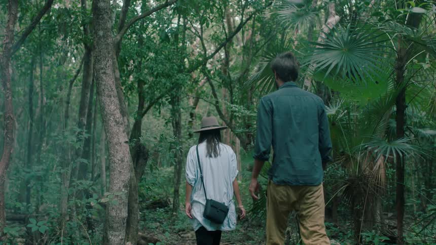 A man and woman walk through a forest together