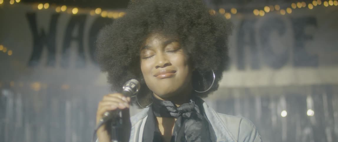 A woman gestures as she sings into a microphone on stage