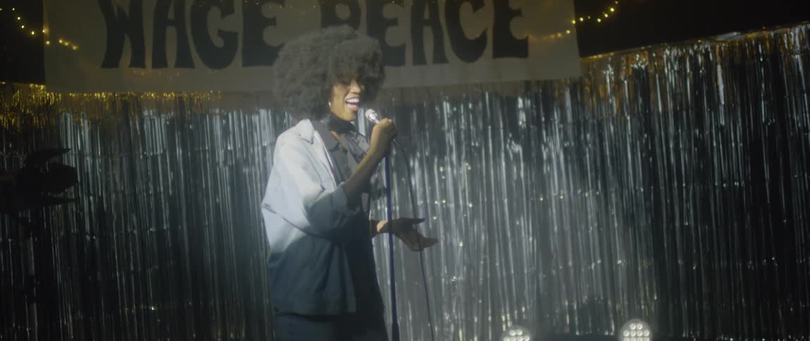 A woman with poofy hair sings on stage