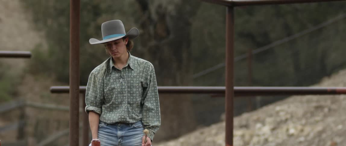 A cowboy stands outside wearing a hat