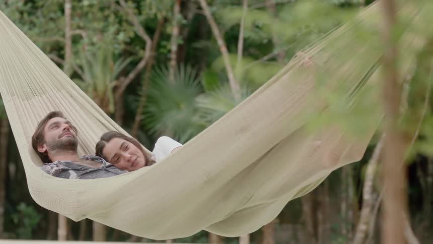 Man and woman lying and talking in hammock outdoors in between trees