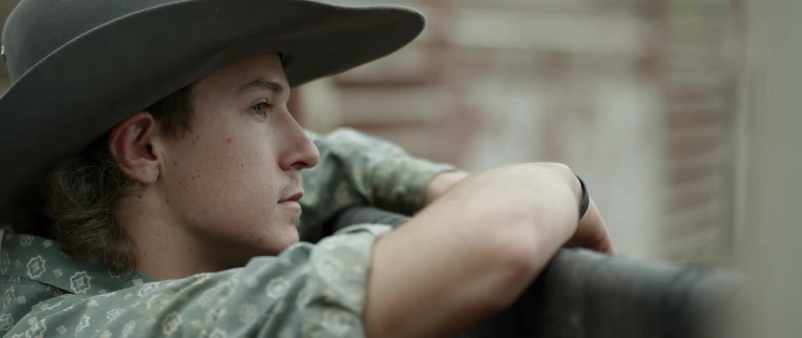 Young man leans on fence while watching what is happening