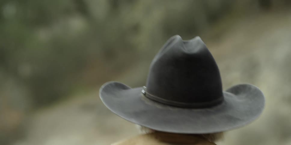A man is wearing a stetson hat as he walks outside during the day
