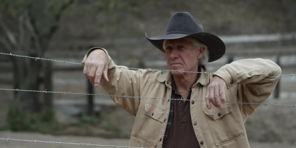 A cowboy hangs his arms on the barbed wire fence