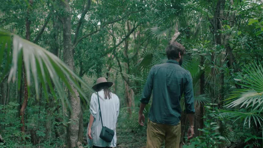 A man and woman walk through a tropical forest