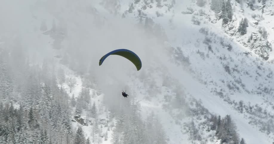A person is paragliding around the snowy mountain