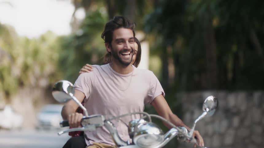 A woman riding on the back of a motorcycle briefly covers the drivers eyes
