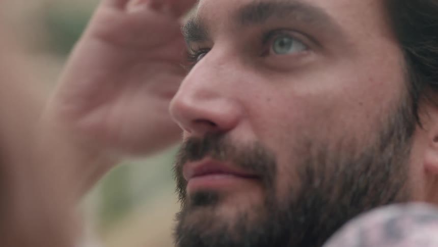A bearded man with blue eyes ruffles his hand through his hair