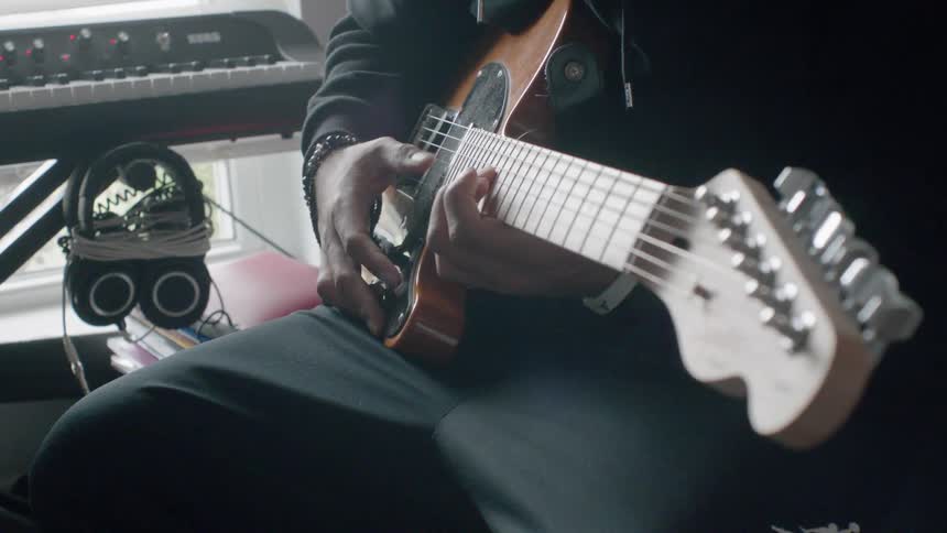 A man sitting next to a keyboard plays the guitar