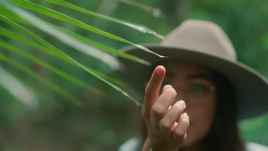 A woman touches the edge of a leaf giving off a drop of water