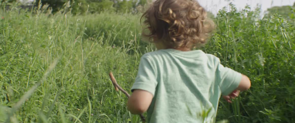 A child walks past the tall grass looking back briefly