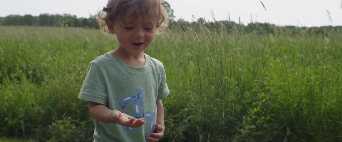 A young boy smiles and holds a bug in a grassy field