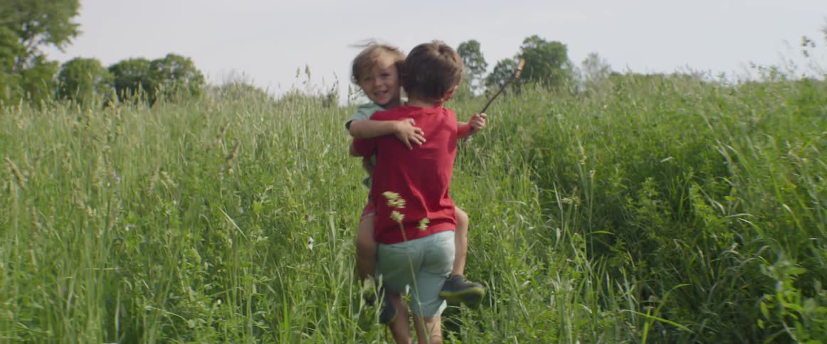 Young boy walks in a field while carrying a baby