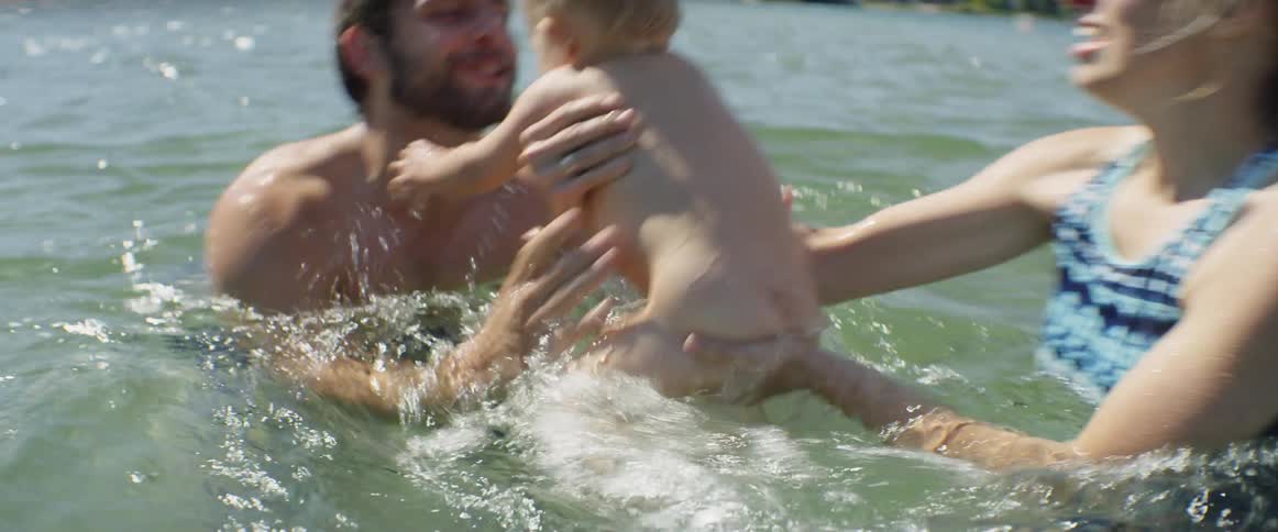 A mother and father swim with a baby in a lake