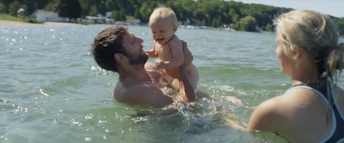A mother and father are swimming and playing with their baby in daylight