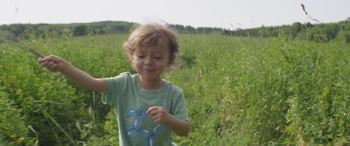 A boy is waving a stick as he is walking in a natural setting in daylight