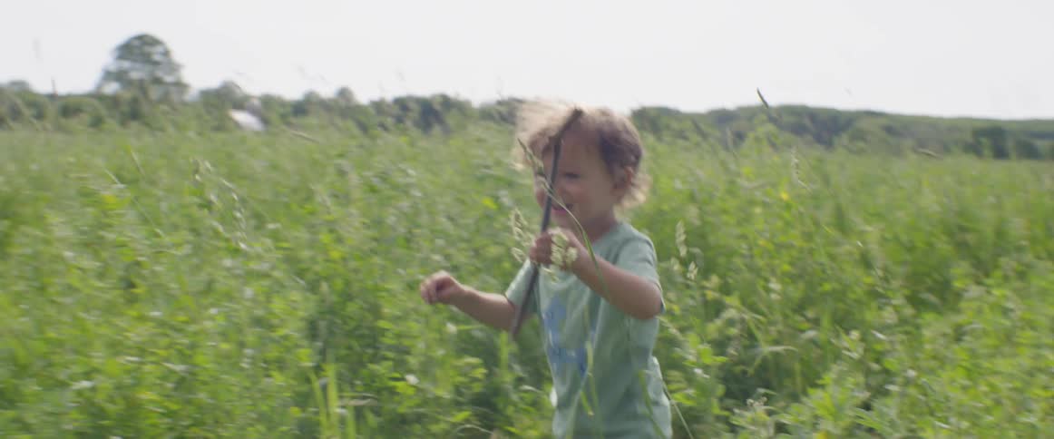 A boy carries a stick walking through the tall grass