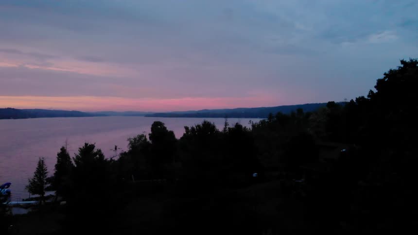 The sun is setting over the lake on a cloudy day
