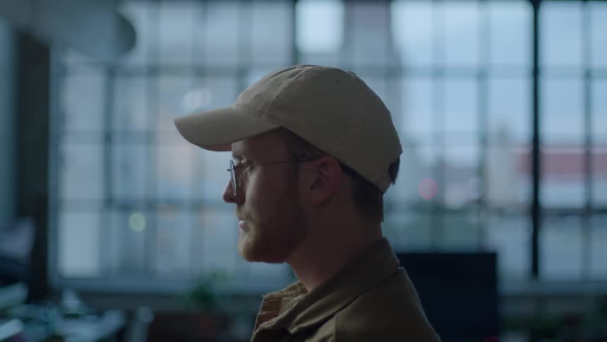 Man wearing a hat and glasses stares ahead