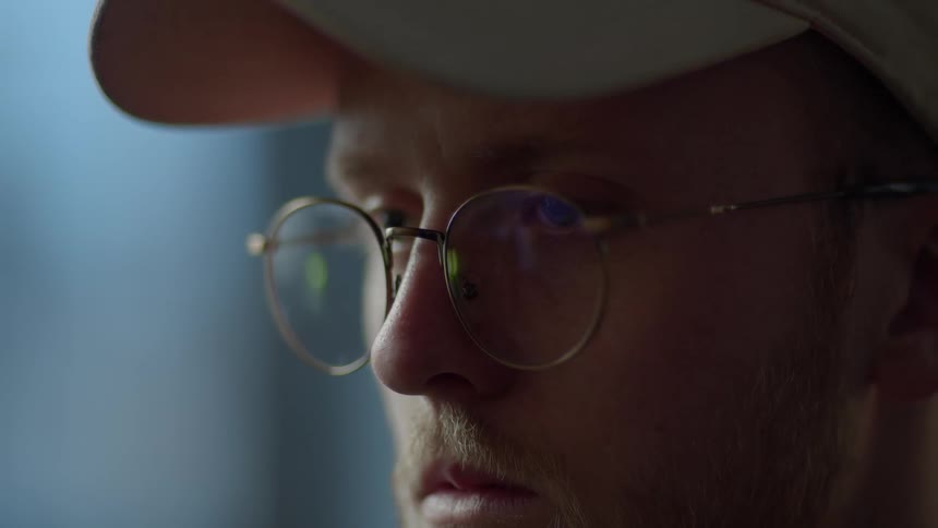 Man wears glasses and a hat as he stares straight ahead