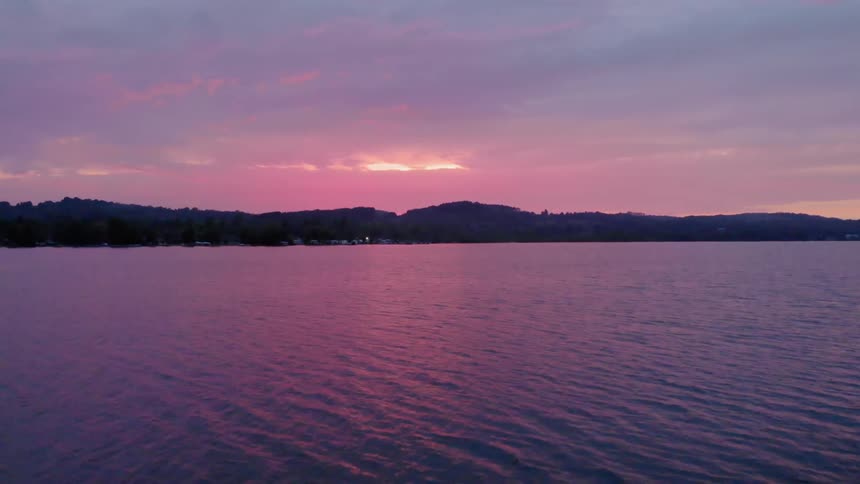 The sky is full of clouds as the sun sets over the water