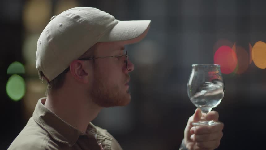 A man is swirling a liquid around inside a glass and examining it