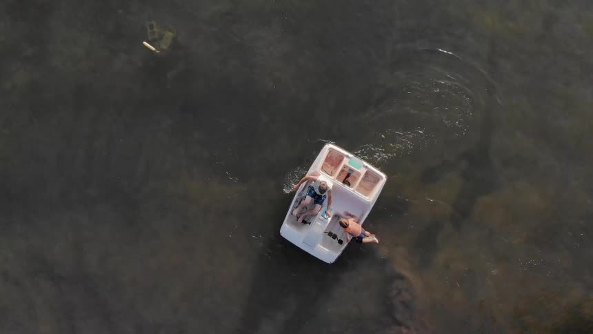 A boy is climbing into a pedal boat as a man operates it during the day