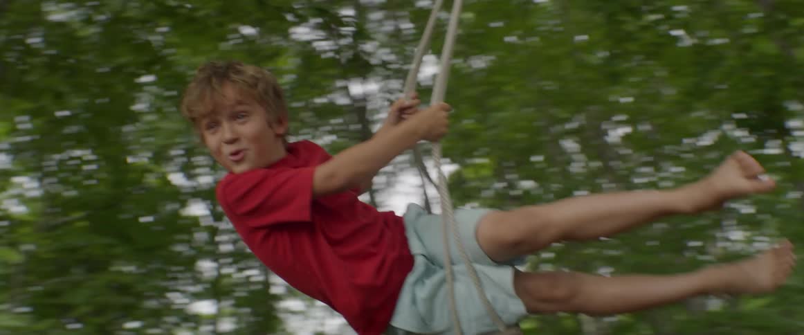 A boy is swinging from a tree in his backyard