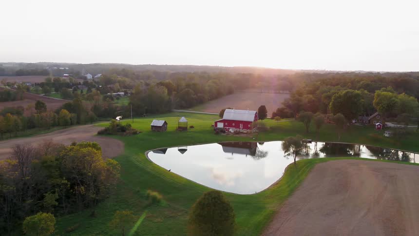 A barn sits next to a pond on a rural farm