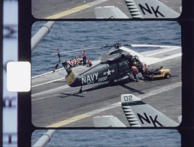 People are working on a navy helicopter on the hangar