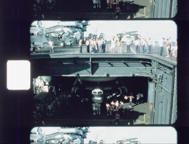 Shirtless men playing a ball game on an aircraft carrier on a sunny day