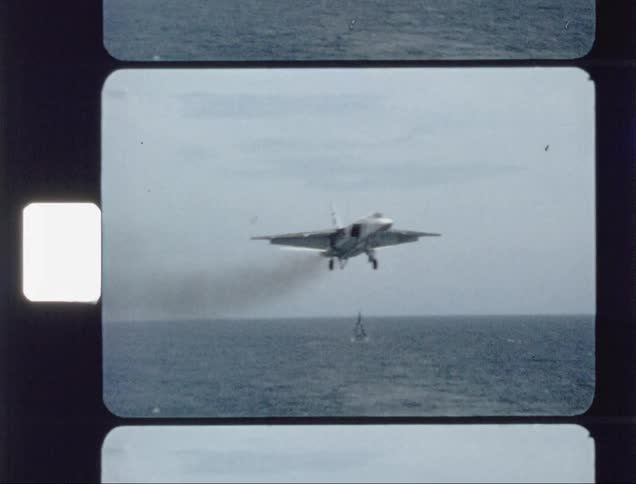 A fighter plane is landing on an aircraft carrier during the day