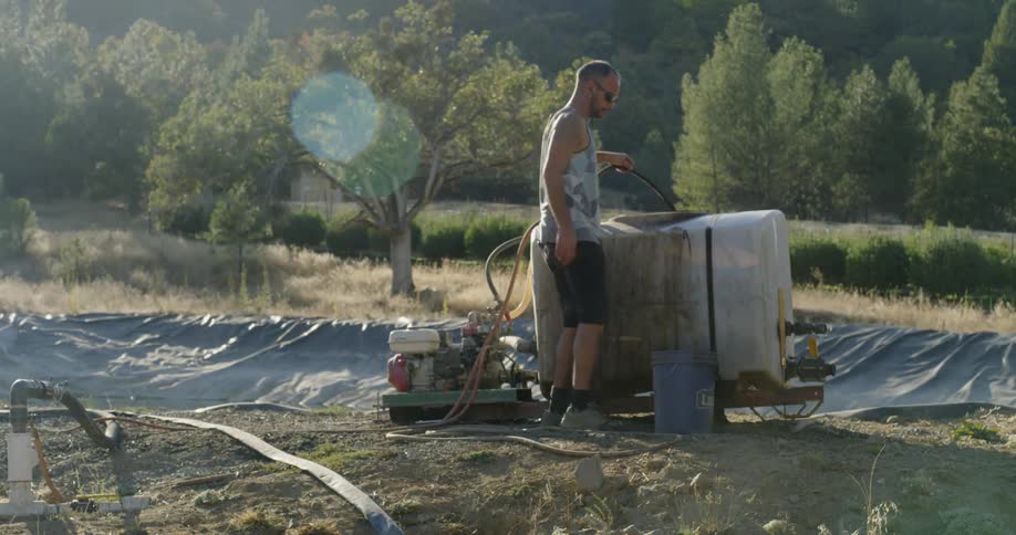 A man empties a bucket and sprays a hose by a machine