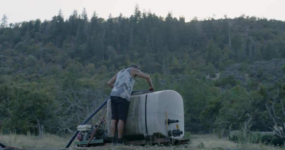 A man leans over a large tank in a rural area