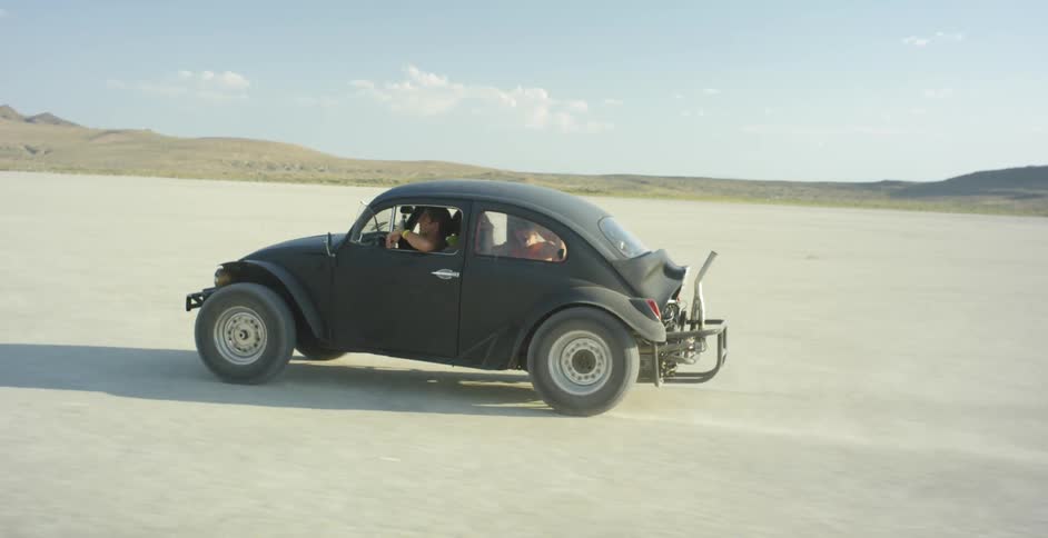 A man drives a volkswagen beetle across a desert