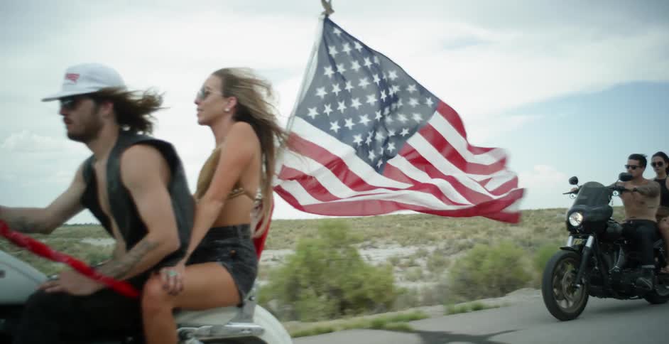 Man and woman ride on a motorcycle with a flag waving on it