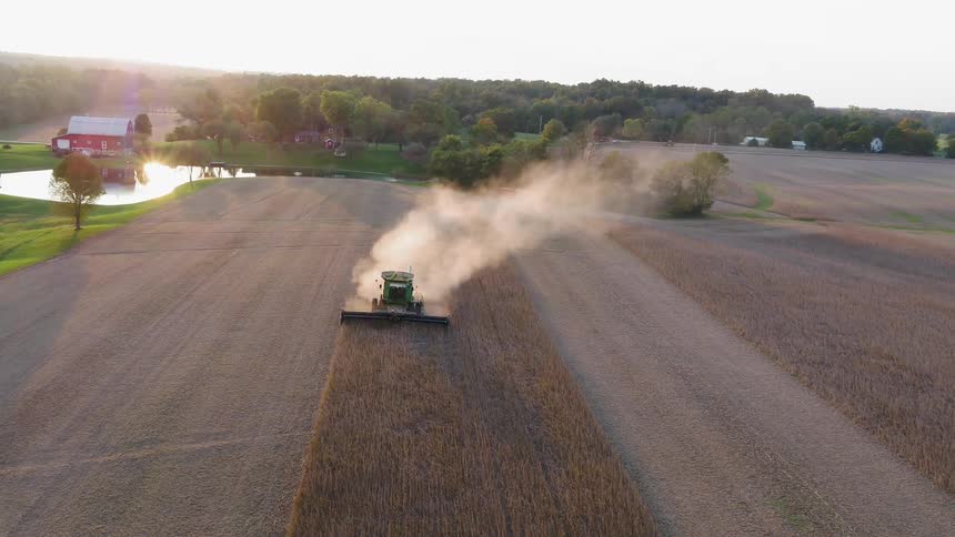 Tractor harvesting and working the field leaving a dust cloud behind