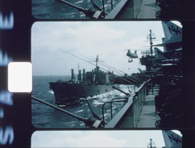 A helicopter is delivering cargo to an aircraft carrier during the day