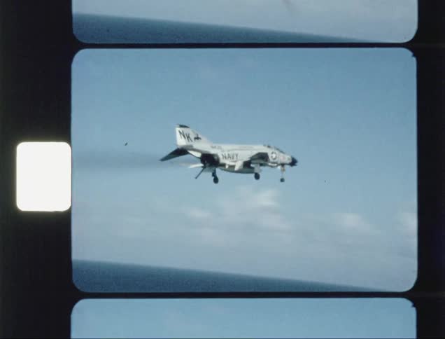 Man photographs a military jet as it flies by the ship