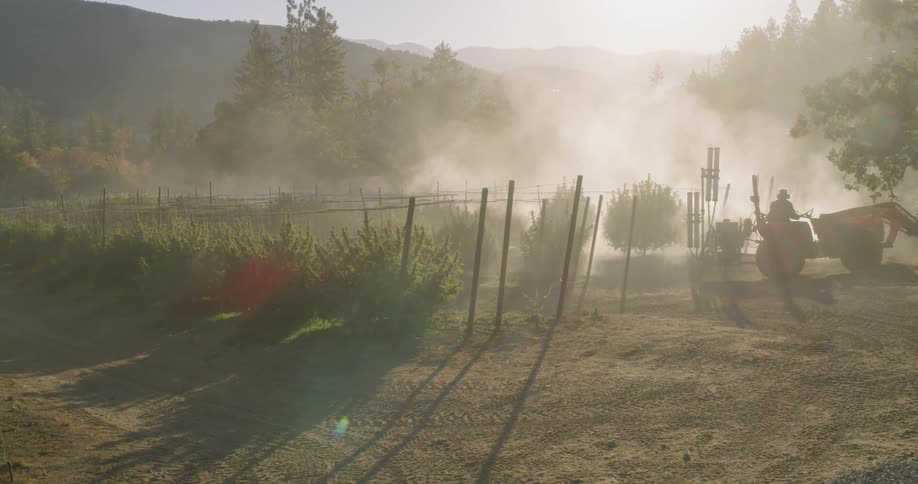 The farmer is driving a vehicle spraying the crops