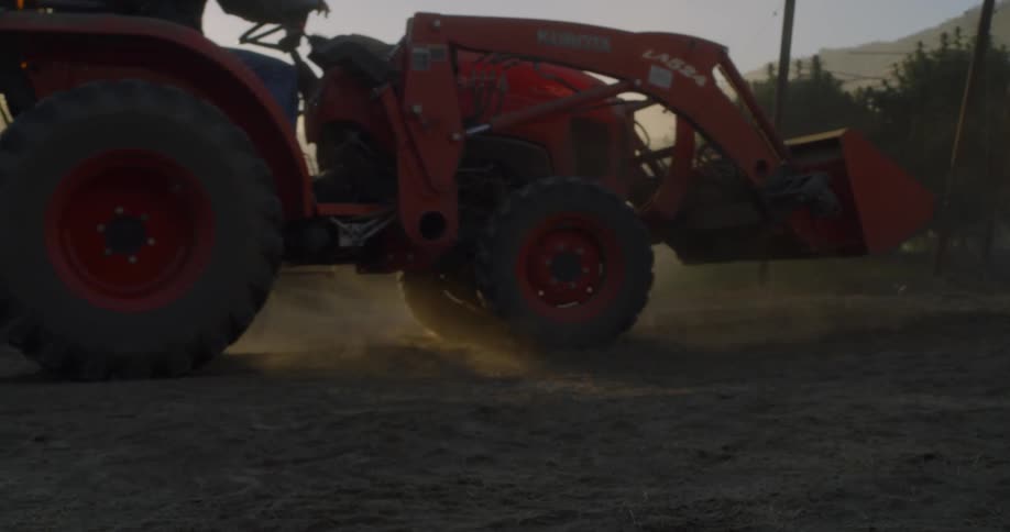 The farm vehicle is being driven backwards at sunrise